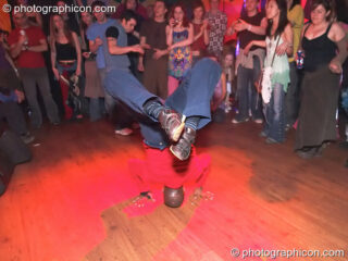 A man stands on his hand in a Capoeira move while being watched by a crowd at The Synergy Project. London, United Kingdom. © 2005 Photographicon