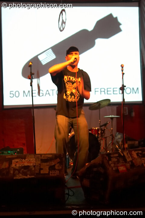 DJ Rubbish raps on the Peace Not War stage with a backdrop of agitprop projections at The Synergy Project. London, United Kingdom. © 2006 Photographicon