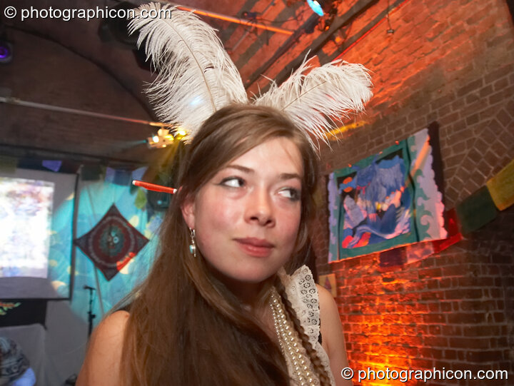 Woman with feathers in her hair takes a sideways glance at The Synergy Project. London, United Kingdom. © 2007 Photographicon
